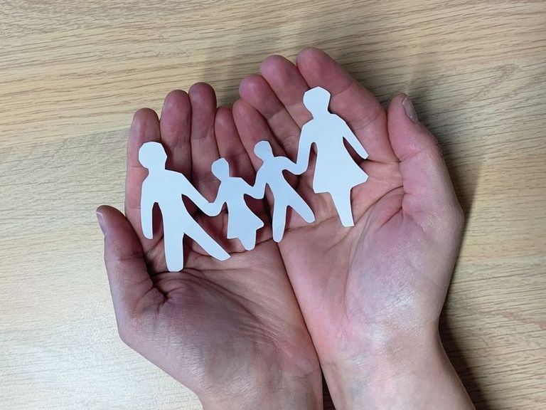 Scherenschnitt-Familie aus Papier liegt in zwei Händen.