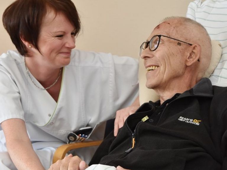 Pflegerin und sterbenskranker Patient lächeln sich an.