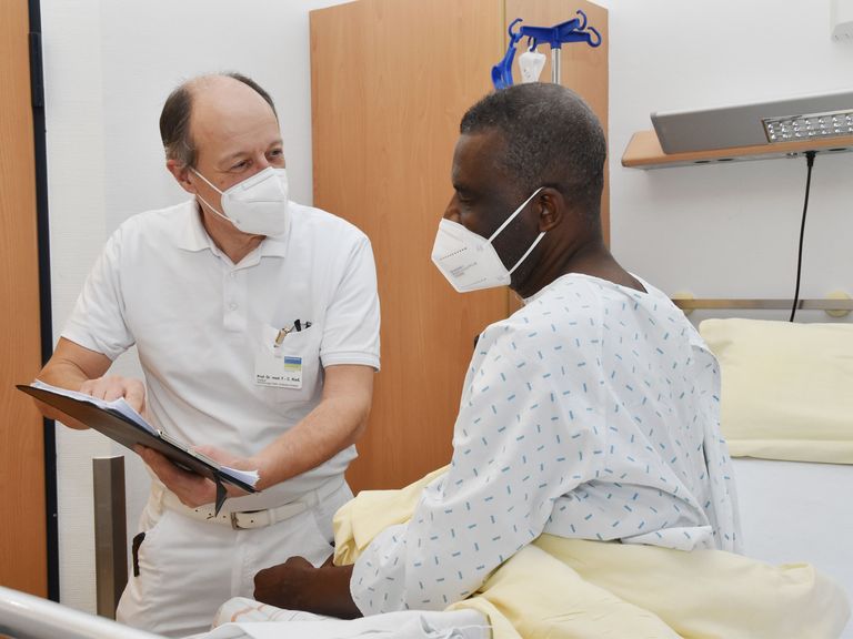 Arzt erläutert seinem Patienten am Krankenbett den Eingriff.