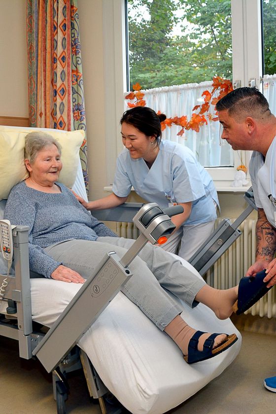 Zwei Pflegekräfte zeigen einer älteren Dame, wie ihr spezielles Aufstehbett funktioniert.